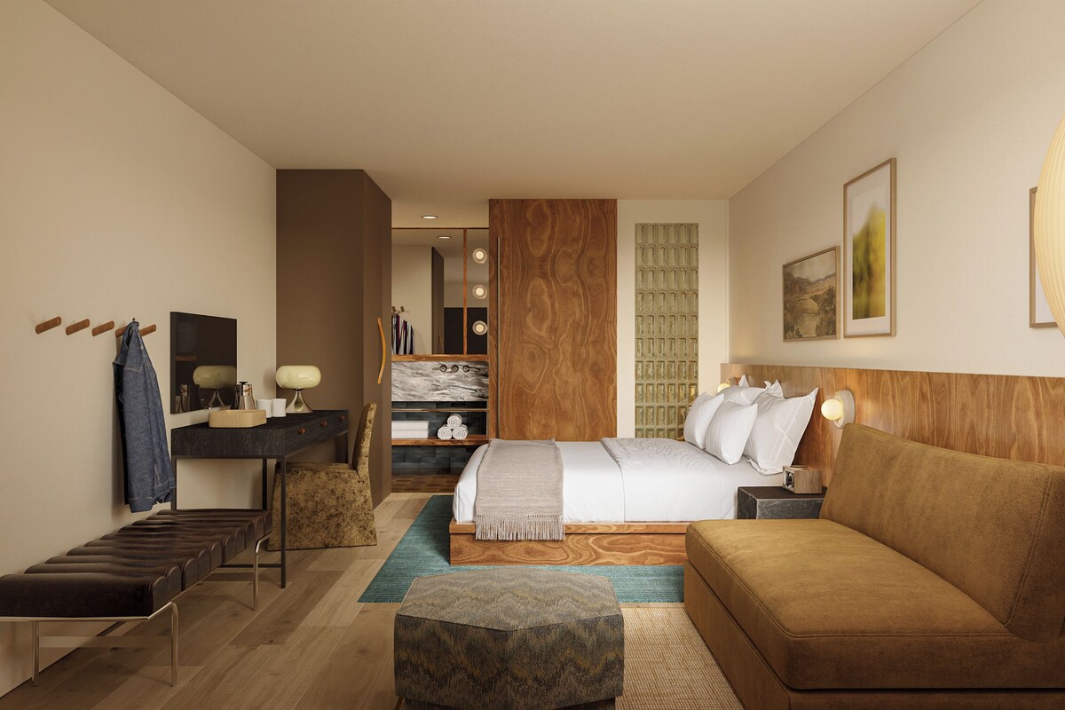 A modern hotel room with a bed, a sofa, a desk, and a bathroom.