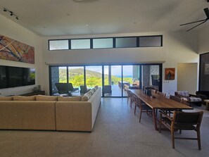 A modern living room with a large sofa, dining table, and chairs, a TV, and a painting.