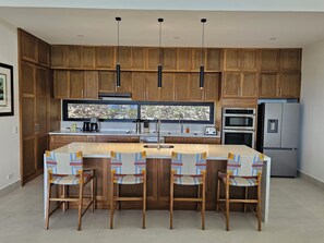 A modern kitchen with wooden cabinets, a central island with bar stools, and stainless steel appliances.