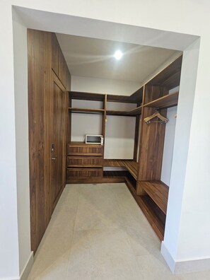 Un vestidor con estantes de madera, una barra para colgar ropa y un microondas.