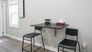 A room with a kitchen counter, two chairs, a potted plant, and a framed quote on the wall.