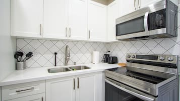Cozinha com armários brancos, pia de aço inoxidável, micro-ondas e forno.