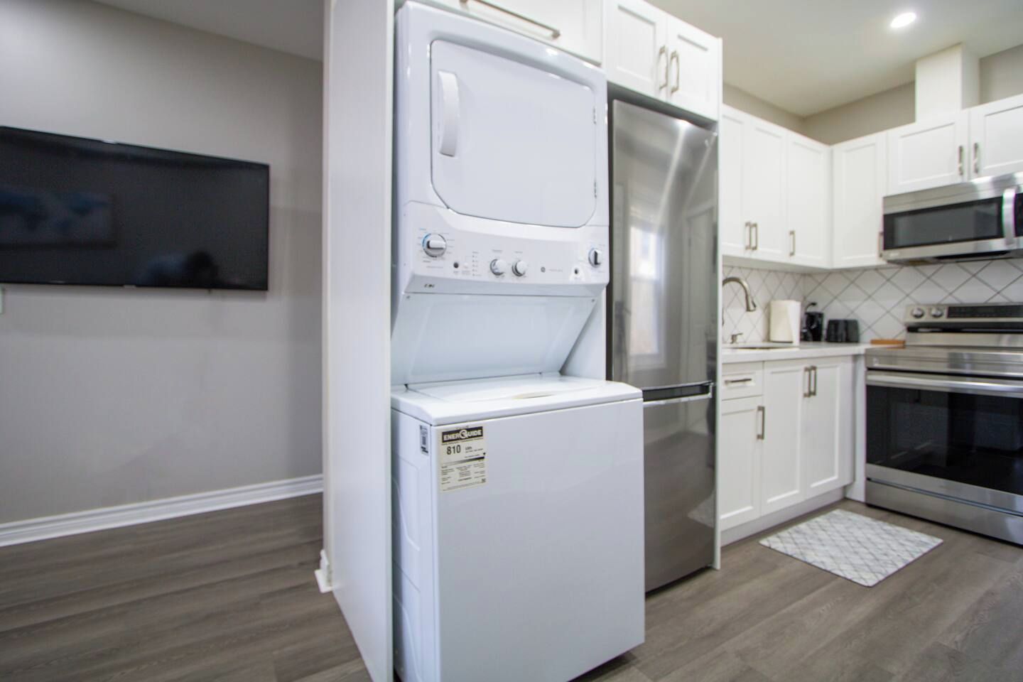 A compact kitchen with white cabinetry, a built-in washer and dryer, stainless steel appliances, and a tiled backsplash.