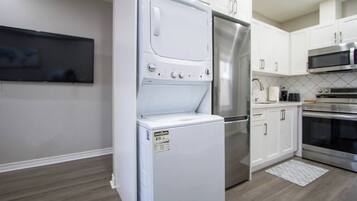 A compact kitchen with white cabinetry, a built-in washer and dryer, stainless steel appliances, and a tiled backsplash.