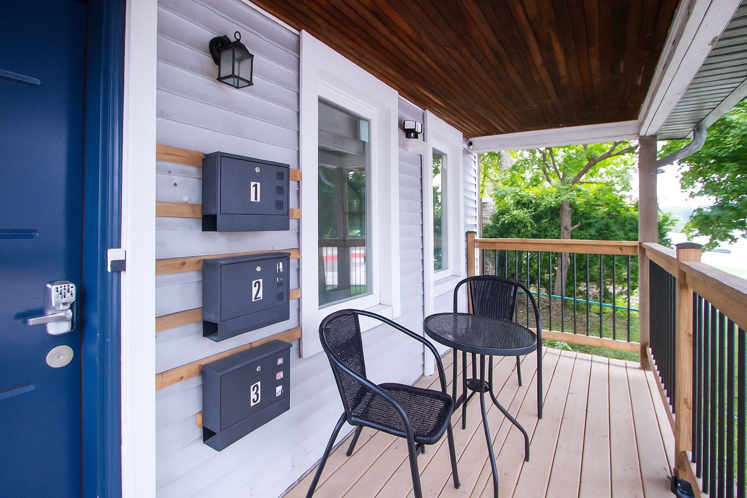 A covered porch with three mailboxes, two chairs, and a wooden railing.