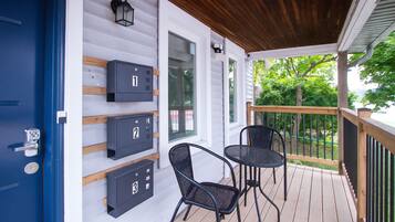 A covered porch with three mailboxes, two chairs, and a wooden railing.
