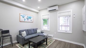 A modern living room with a grey sofa, a coffee table, a world map on the wall, and two windows with blinds.