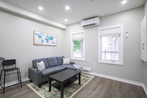Ein modernes Wohnzimmer mit einem grauen Sofa, einem Couchtisch, einer Weltkarte an der Wand und zwei Fenstern mit Jalousien.