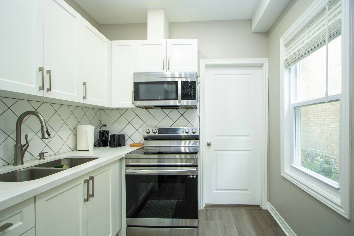 A compact kitchen with white cabinets, a stainless steel range, a microwave, and a built-in oven.