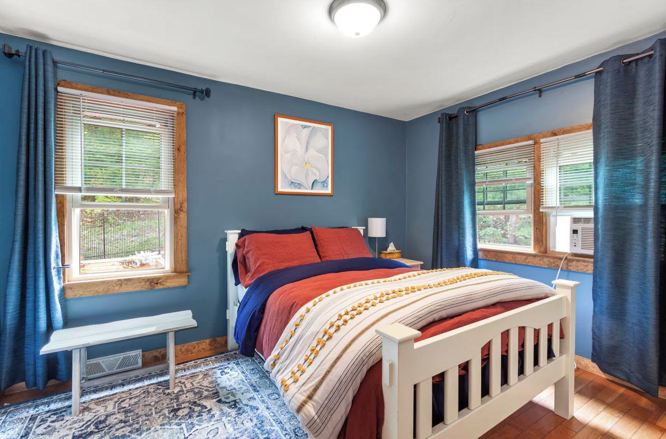 A bedroom with a bed, a bedside table, a bench, and a window with curtains.