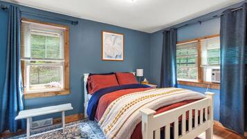 A bedroom with a bed, a bedside table, a bench, and a window with curtains.