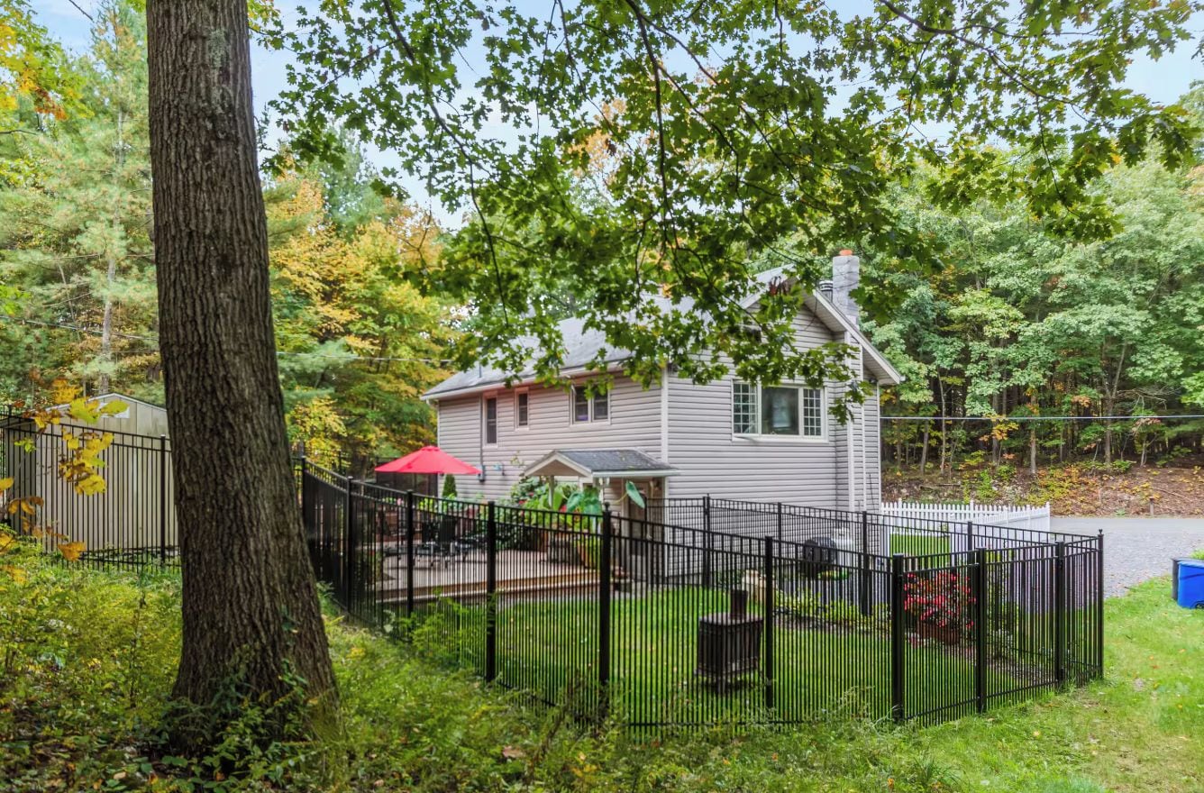 A house with a fenced backyard, surrounded by trees.