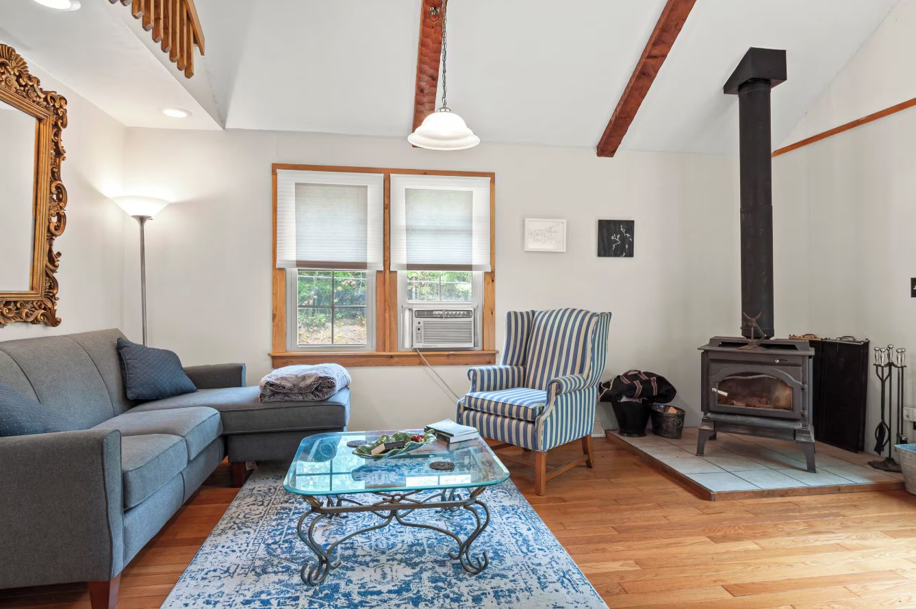A living room with a sofa, armchair, glass coffee table, fireplace, and a large mirror.