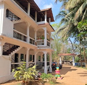 A two-story building with balconies, a staircase, and a garden area with potted plants. - Studio Silent Grove R-6 Couple Choice (Arambol)