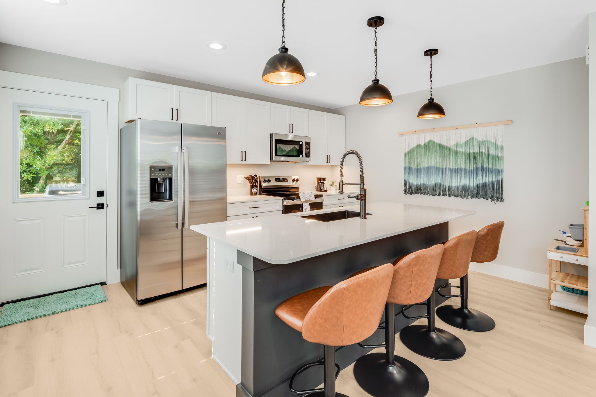 A modern kitchen with a stainless steel refrigerator, a microwave, and a sink. There are three bar stools at the island.