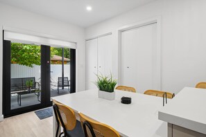A modern dining area with a white table, black chairs, and a potted plant. - The Cove in the Grove Bungalow in Historic Coconut (Miami)
