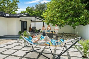 Una hamaca en un patio trasero con terraza, una parrilla y una zona de comedor.