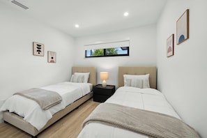 A hotel room with two beds, a window with a view of trees, and a small table with a lamp. - The Cove in the Grove Bungalow in Historic Coconut (Miami)