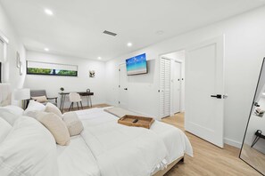 A modern bedroom with a large bed, a desk, and a TV on the wall. - The Cove in the Grove Bungalow in Historic Coconut (Miami)