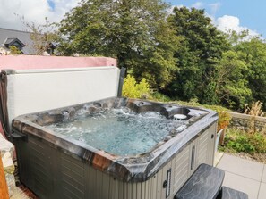 A hot tub with a wooden exterior, surrounded by greenery and a stone wall. - Ty Mawr (Criccieth)