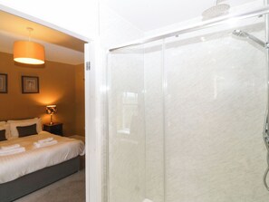 Ein Hotelzimmer mit einer gläsernen Dusche, einem Bett mit ordentlich gefalteten Handtüchern und einer Nachttischlampe.