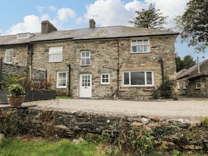A stone house with a gravel driveway, a wooden fence, and a potted plant. - Ty Mawr (Criccieth)