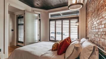 A bedroom with a bed, a window with blinds, a brick wall, and a ceiling light fixture.