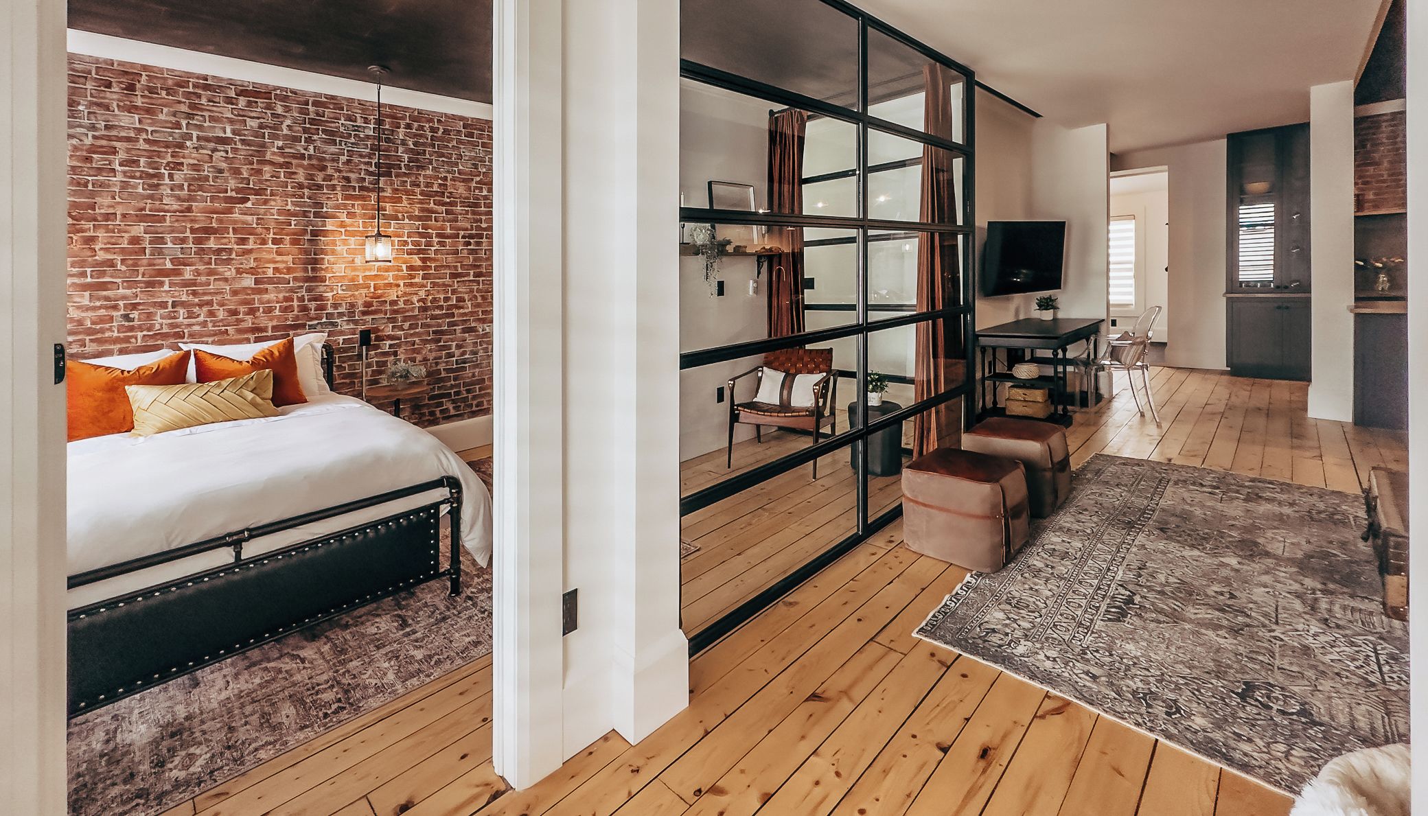 Ein Schlafzimmer mit Backsteinwand, einem Bett mit Kissen, einem Nachttisch und einem Fenster mit Vorhängen.