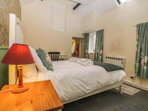 Ein Schlafzimmer mit einem Bett, einem hölzernen Nachttisch, einer roten Lampe, einem Sessel, einer Heizung und Vorhängen.