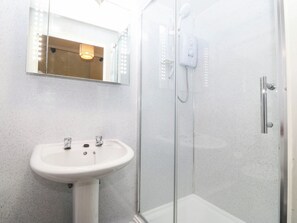 Ein Badezimmer mit einer Duschkabine, einem weißen Waschbecken und einem beleuchteten Spiegel.
