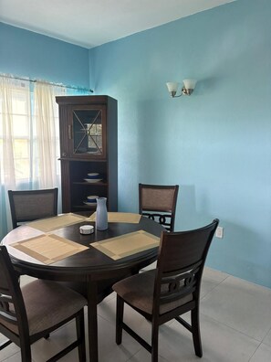 A dining area with a round table, four chairs, a cabinet, and a wall-mounted light fixture. - Manna Heights. Perfect 2-bedroom apartment with AC in peaceful Bolands. (Bolands)