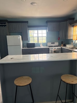 A modern kitchen with grey cabinets, a white refrigerator, a stove, and a large island with two stools. - Manna Heights. Perfect 2-bedroom apartment with AC in peaceful Bolands. (Bolands)
