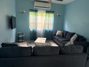 Ein Wohnzimmer mit einem dunkelgrauen Sofa, einem Couchtisch und einem an der Wand montierten Fernseher.