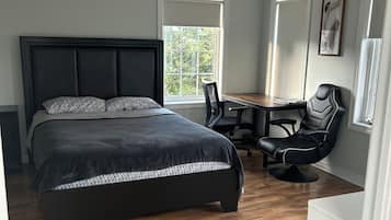 Un dormitorio con una cama grande, un escritorio, dos sillas y una ventana.