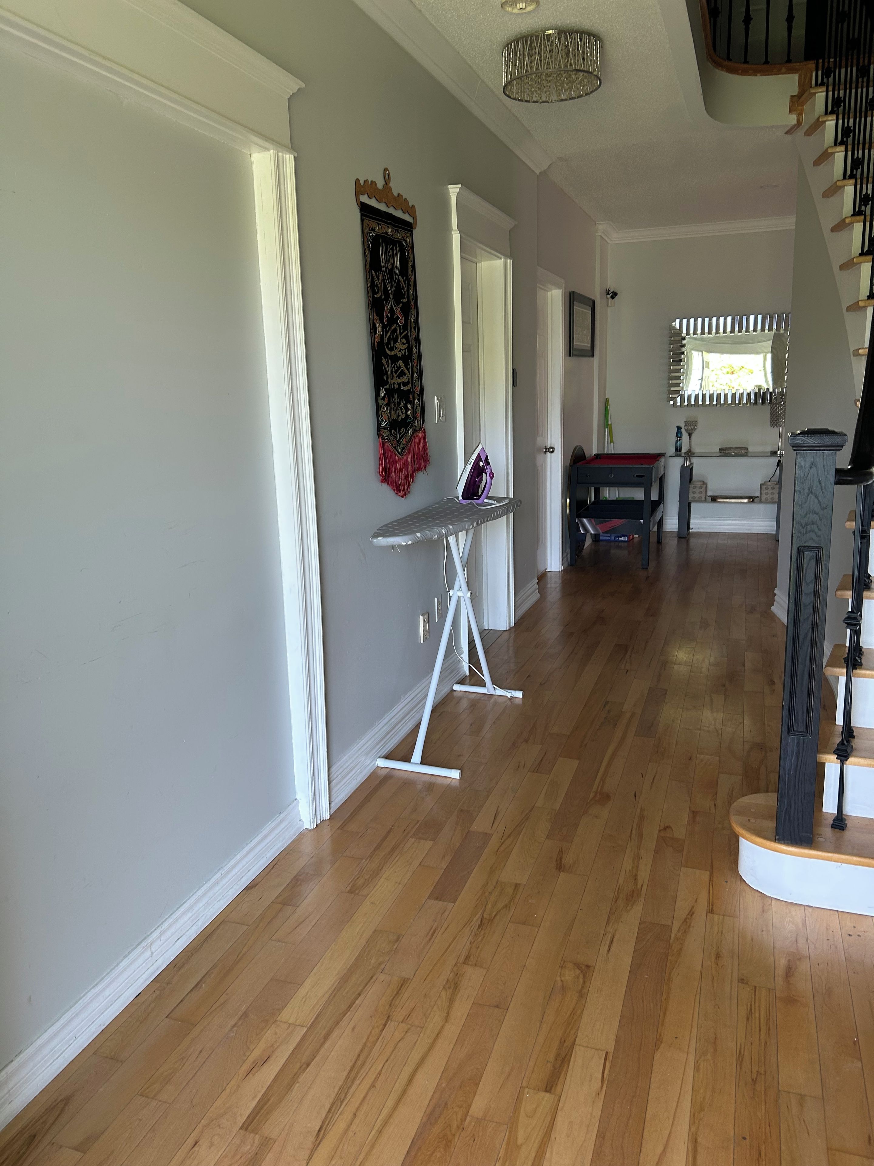 Un couloir avec un plancher en bois, une planche à repasser blanche et un escalier doté d’une rampe en bois.
