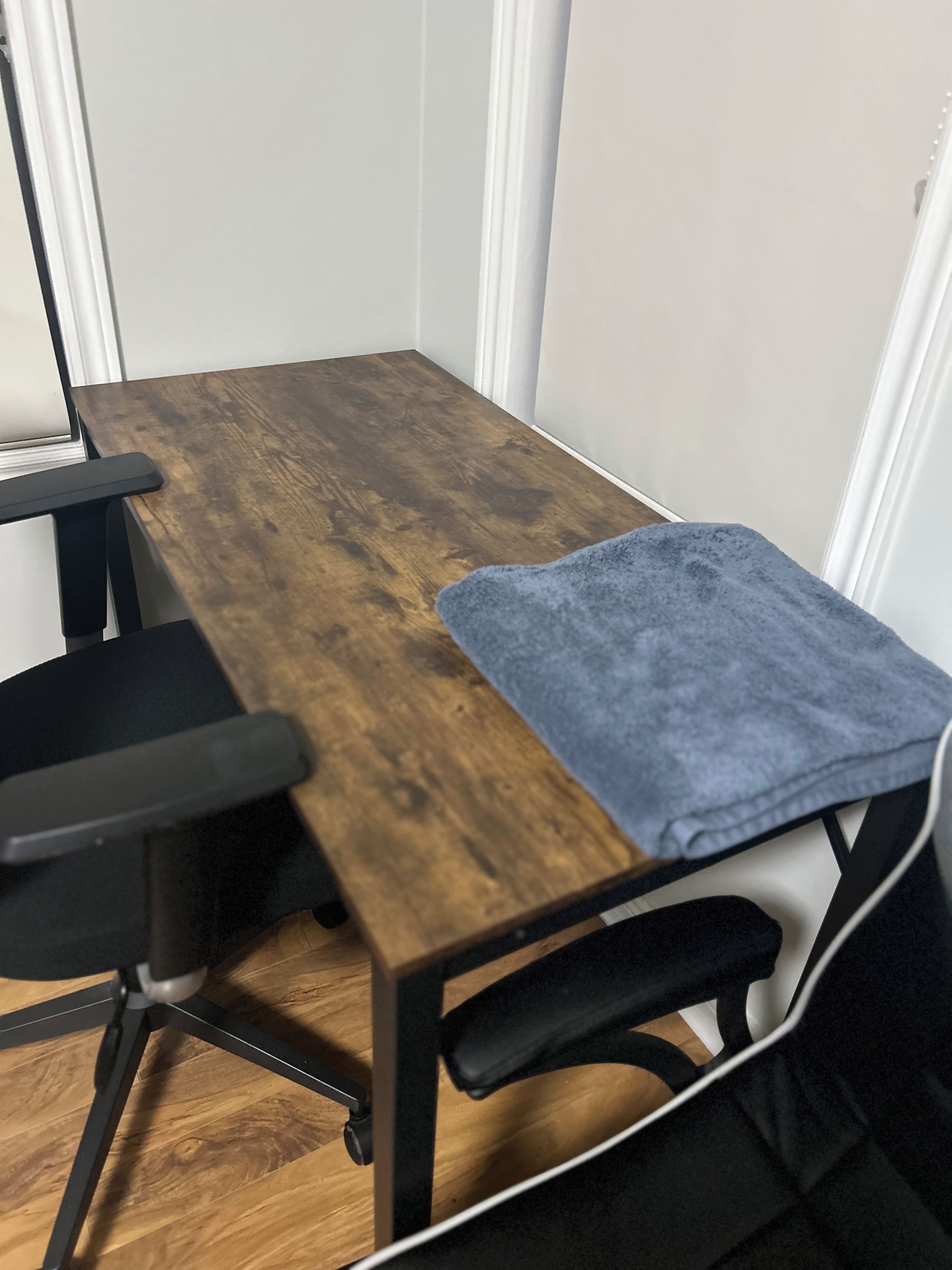 Un bureau en bois, une chaise de bureau noire, un tissu bleu sur le côté droit et des murs blancs.