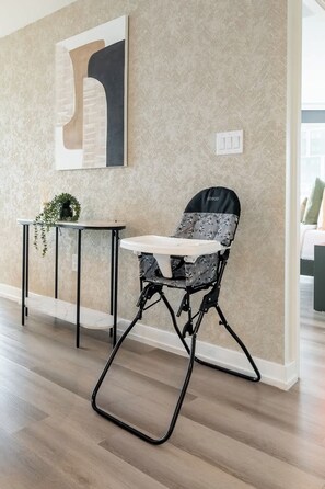 A high chair with a black frame and a patterned cushion, positioned next to a small table with a plant. - Waterfront 2BR Suite, Luxury Views & Parking | Parking Available (Toronto)