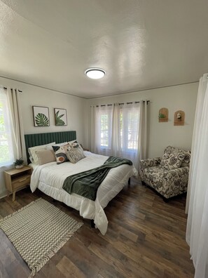 Ein Schlafzimmer mit Bett, Nachttisch, Stuhl und Vorhängen.