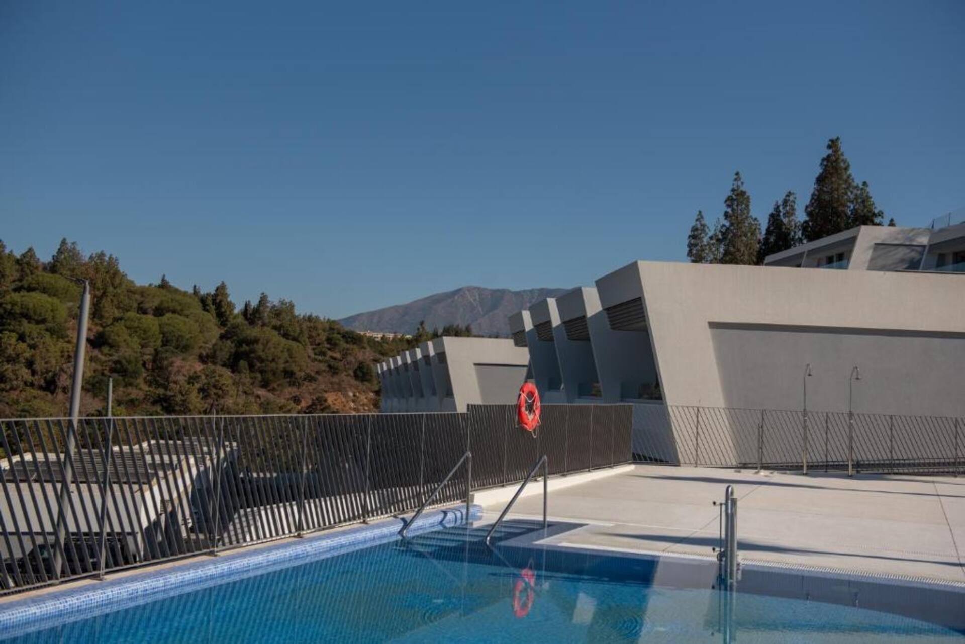 A swimming pool with a lifebuoy, surrounded by a fence, and modern architecture in the background.