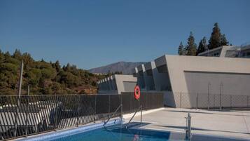 A swimming pool with a lifebuoy, surrounded by a fence, and modern architecture in the background.