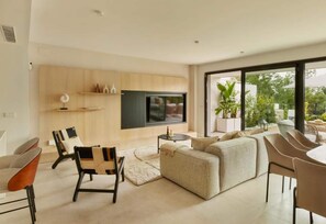 Una sala de estar moderna con televisor grande, asientos cómodos y vistas al exterior.