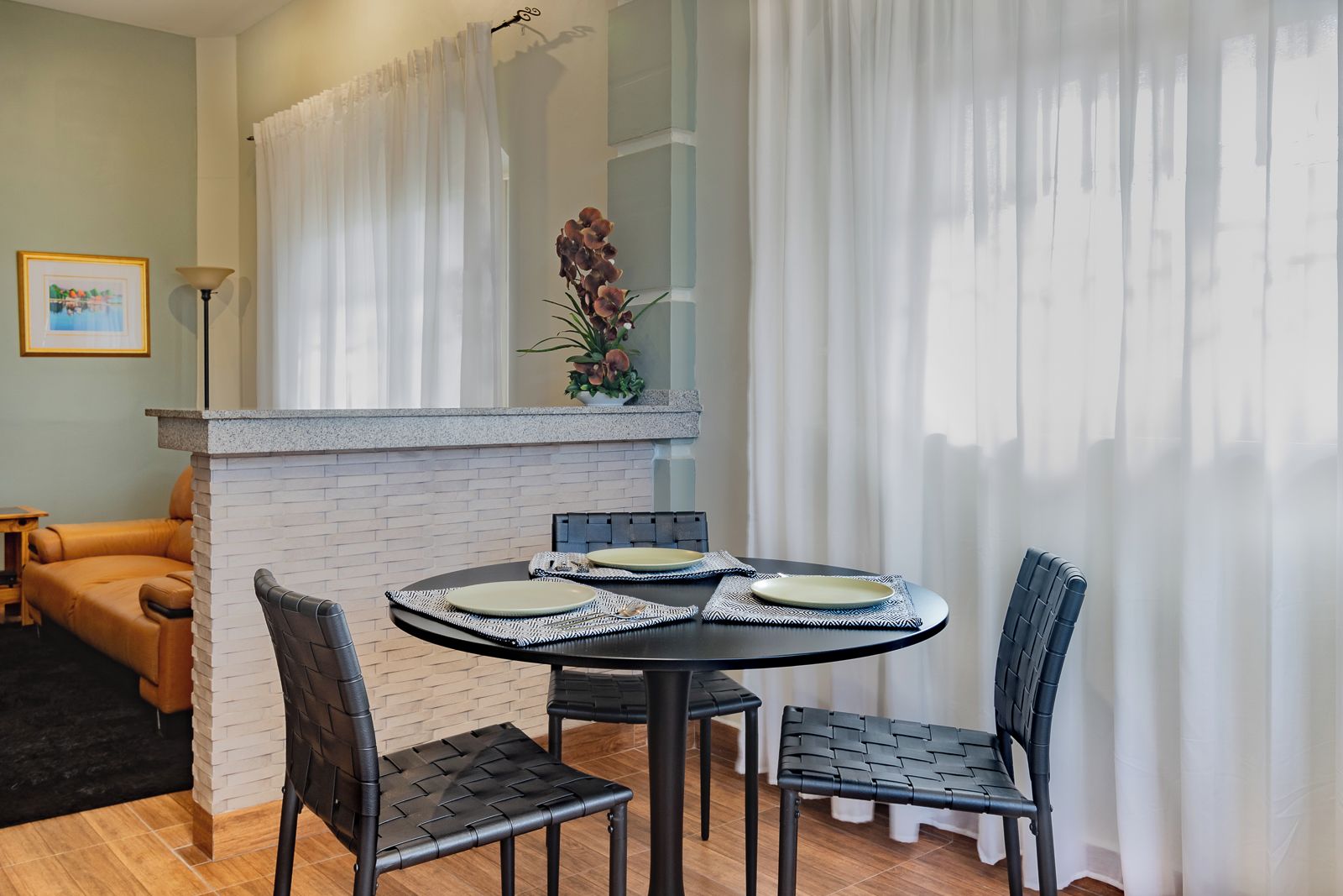 Un espace repas comprenant une table ronde, quatre chaises et une cloison en briques blanches.