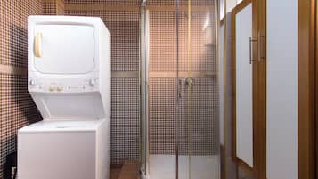 A compact bathroom with a washing machine, a shower enclosure, and a wooden cabinet.
