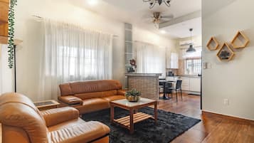 A modern living room with a leather sofa, a coffee table, and a dining area with a kitchen in the background.