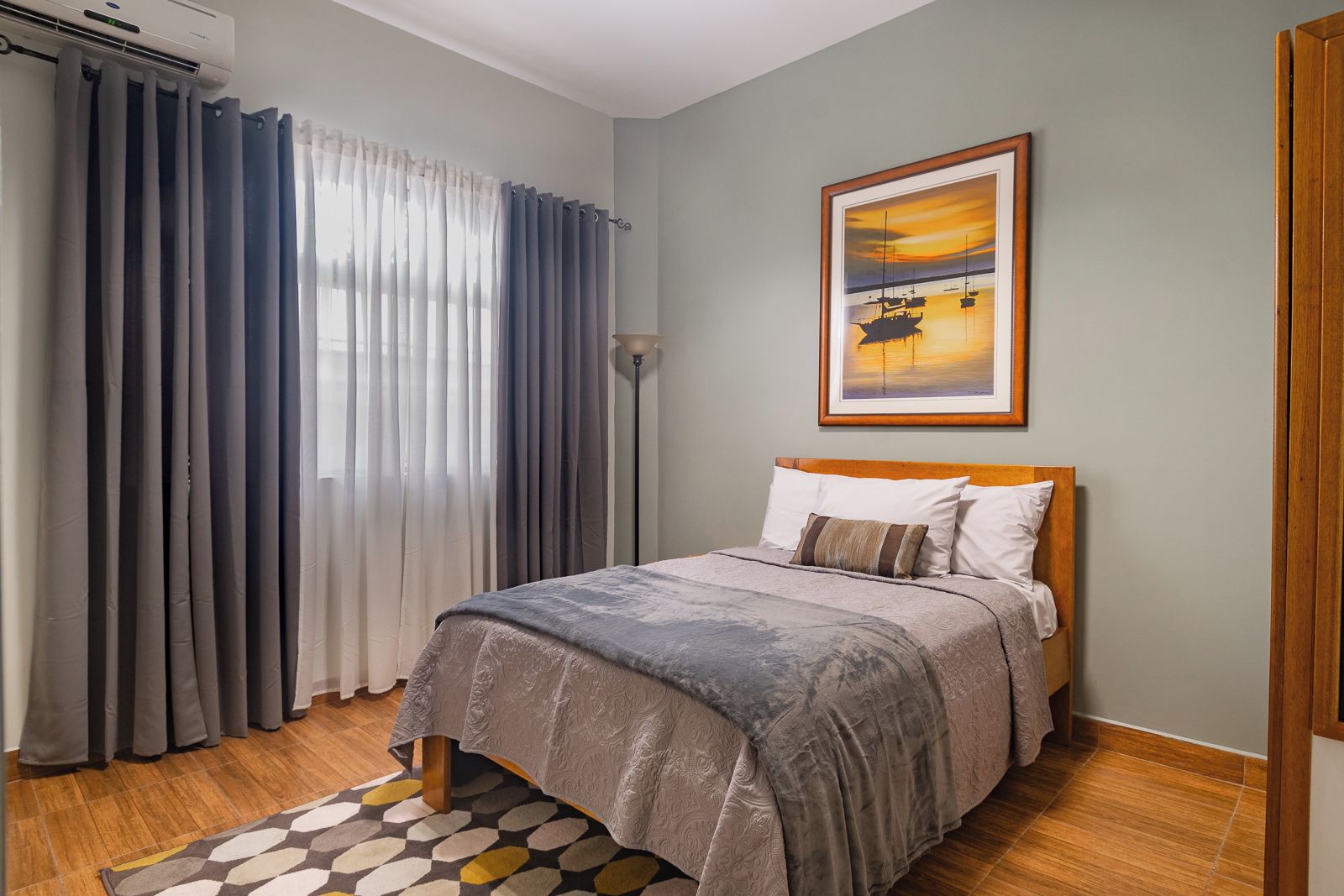 A bedroom with a bed, curtains, a painting, and a patterned rug.