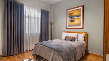 A bedroom with a bed, curtains, a painting, and a patterned rug.