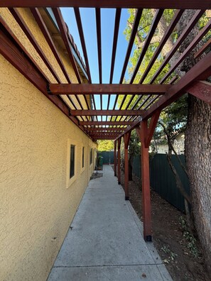 A covered walkway with a wooden pergola, a concrete path, and a tree on the right. - Family Getaway with pool & Gym (Chico)