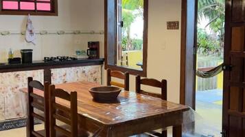Mesa de jantar de madeira com cadeiras, um prato e bancada de cozinha com fogão a gás e cafeteira.