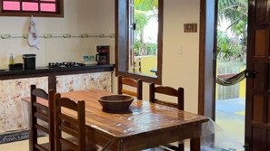 A wooden dining table with chairs, a bowl, and a kitchen counter with a gas stove and coffee maker. - Pousada Cumurumaré (Cumuruxatiba)