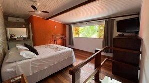 A bedroom with a bed, a television, a ceiling fan, a window with curtains, and a wooden staircase. - Pousada Cumurumaré (Cumuruxatiba)